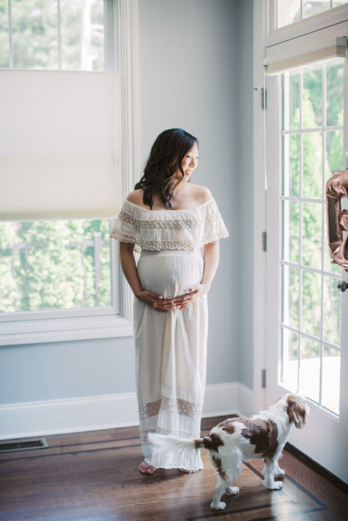 a mother is holding her pregnant belly while looking out of the the french doors of her home during her at home maternity session