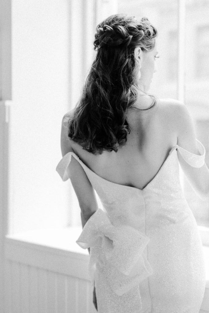 Bride looks longingly out of NYC loft window in elegant gown