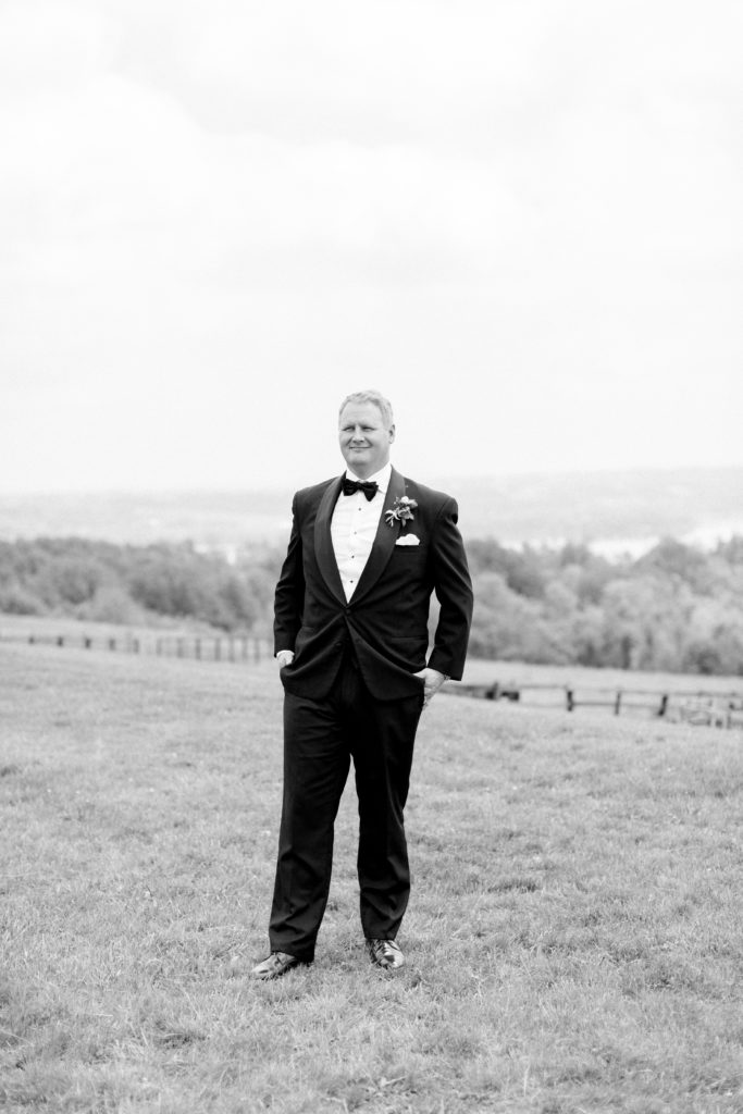 groom stands on hill overlooking farmland at Lauxmont farms wedding