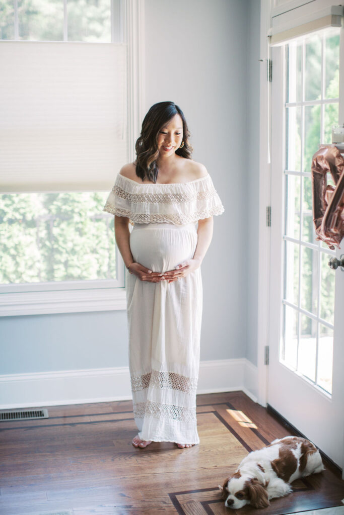 a mother is holding her pregnant belly and smiling while looking standing in her home during her at home maternity session