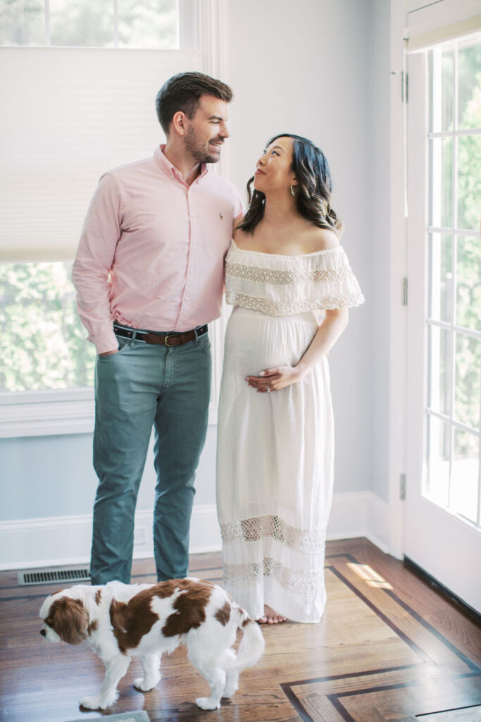 couple embrace and smile at each other during their at home maternity session as a family