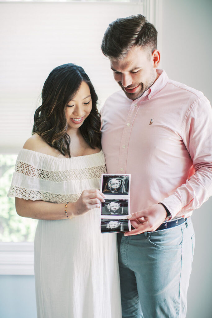 couple hold up sonogram of their baby while embracing during their cozy at home maternity session captured by central pa photographer writer & beloved photography
