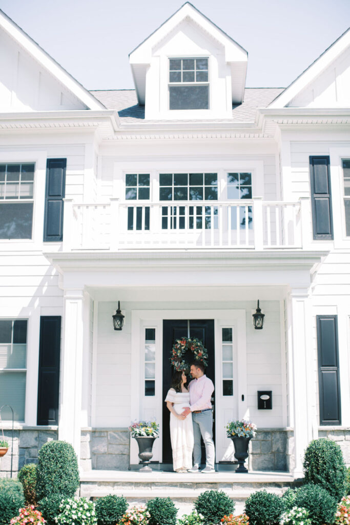 Couple embrace in front of their home during their cozy at home maternity session