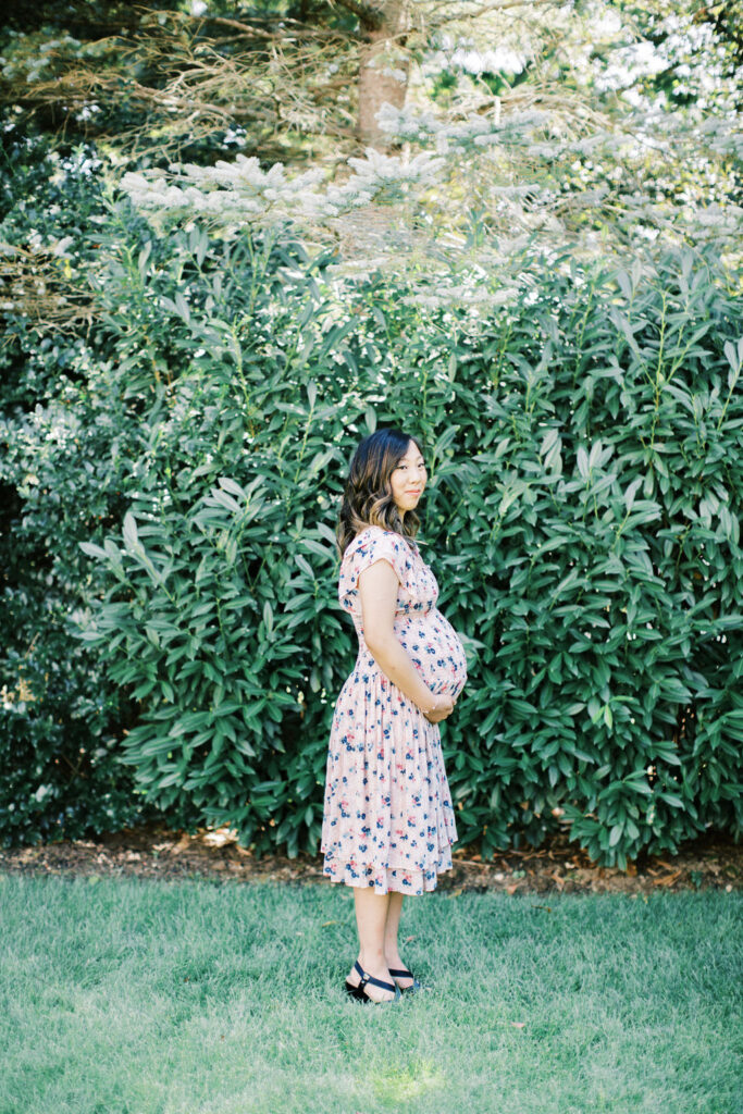 woman stands in her yard in a pink dress during her cozy at home maternity session
